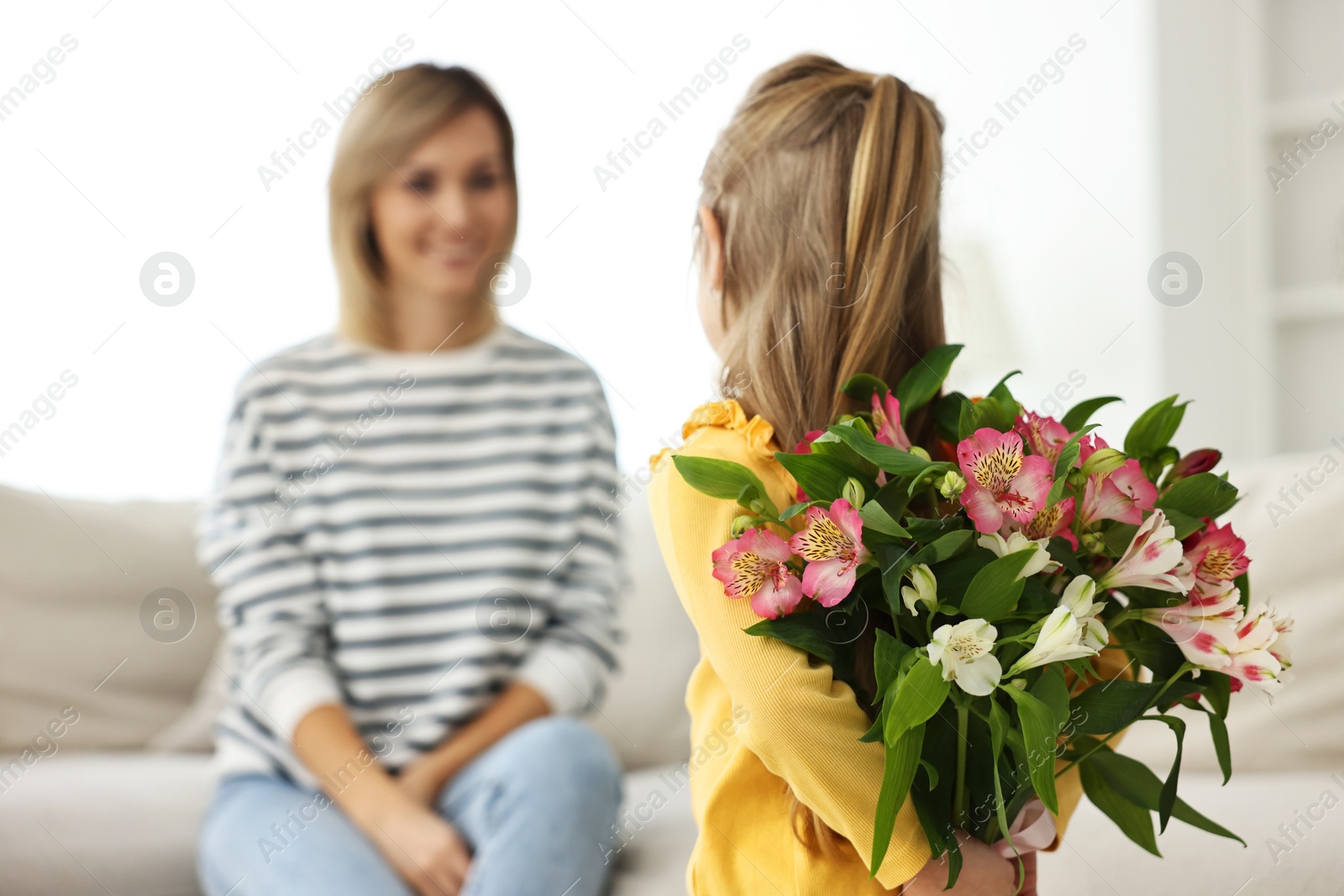 Photo of Little girl hiding bouquet of alstroemeria flowers for mom at home, selective focus. Happy Mother's Day