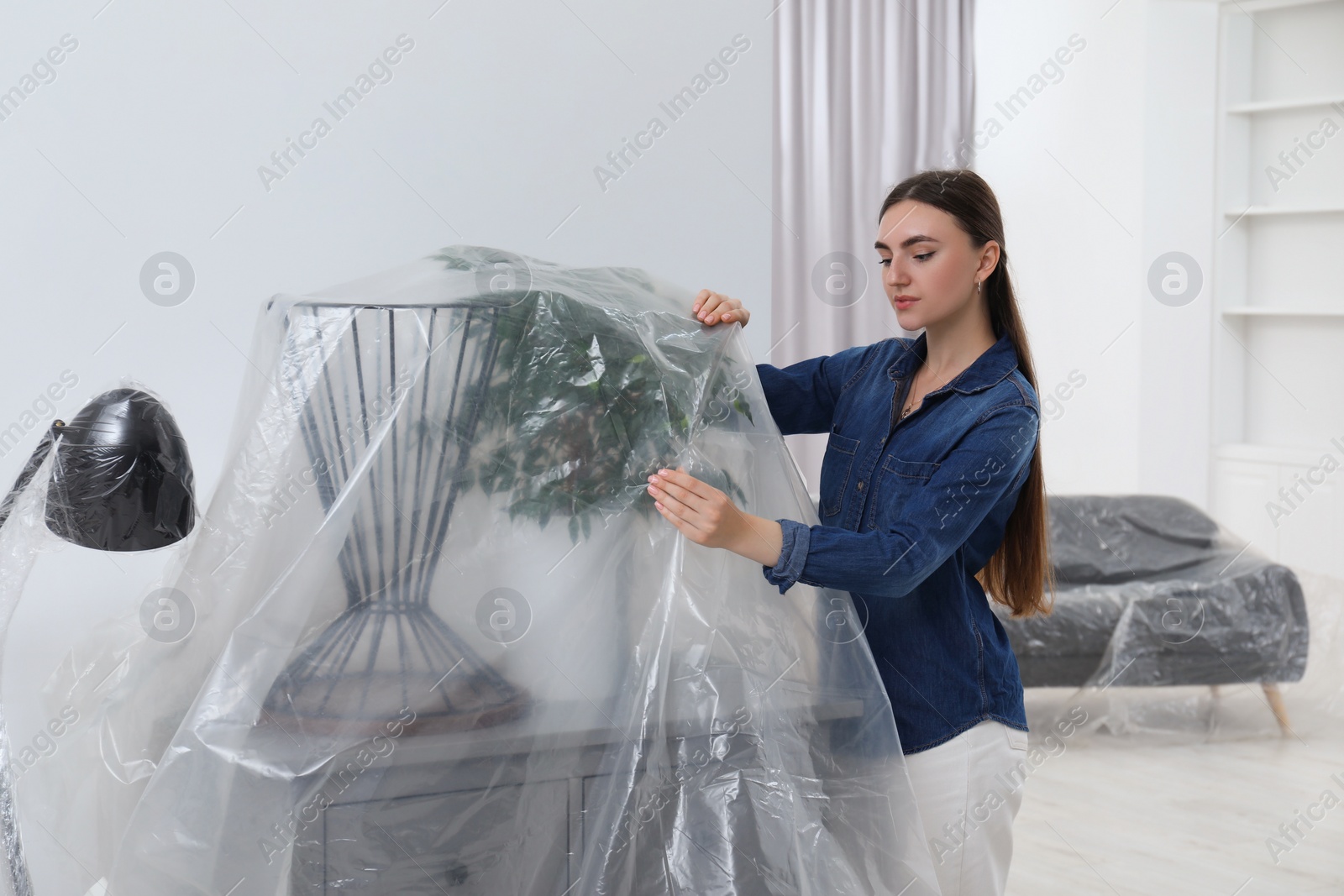 Photo of Young woman putting plastic film away from furniture at home