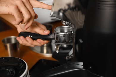 Photo of Barista pouring milled coffee from grinding machine into portafilter, closeup