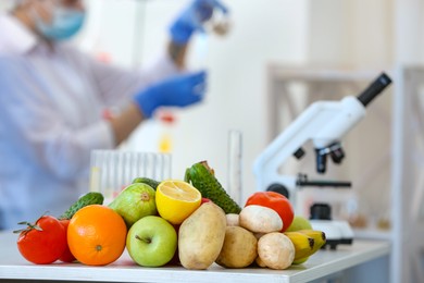 Fresh vegetables, fruits on table and scientist proceeding quality control in laboratory