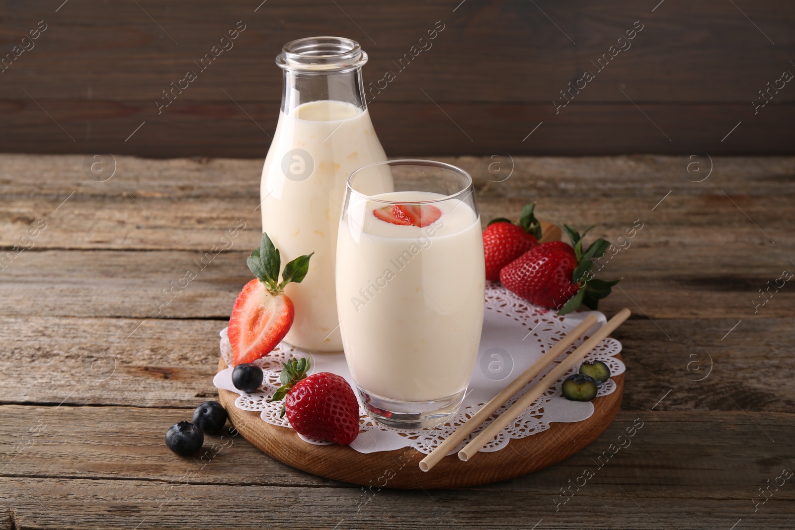 Photo of Tasty yogurt in glass, bottle, straws and berries on wooden table