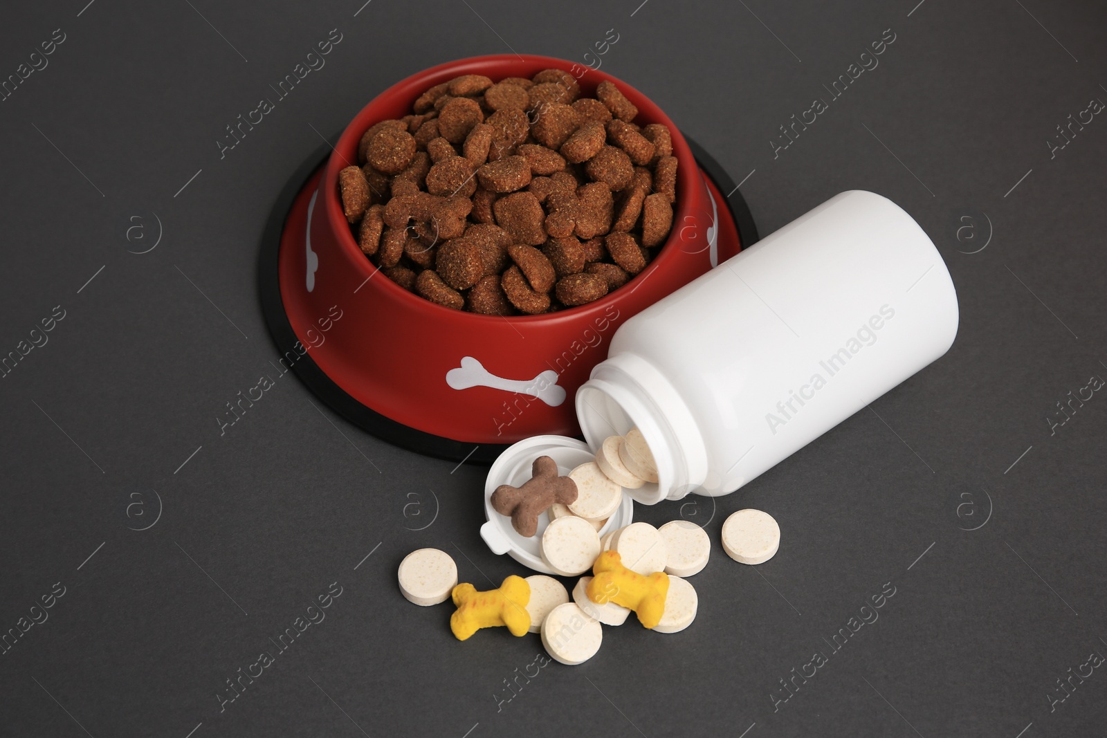 Photo of Bottle with vitamins and dry pet food in bowl on grey background, above view