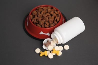 Photo of Bottle with vitamins and dry pet food in bowl on grey background, above view