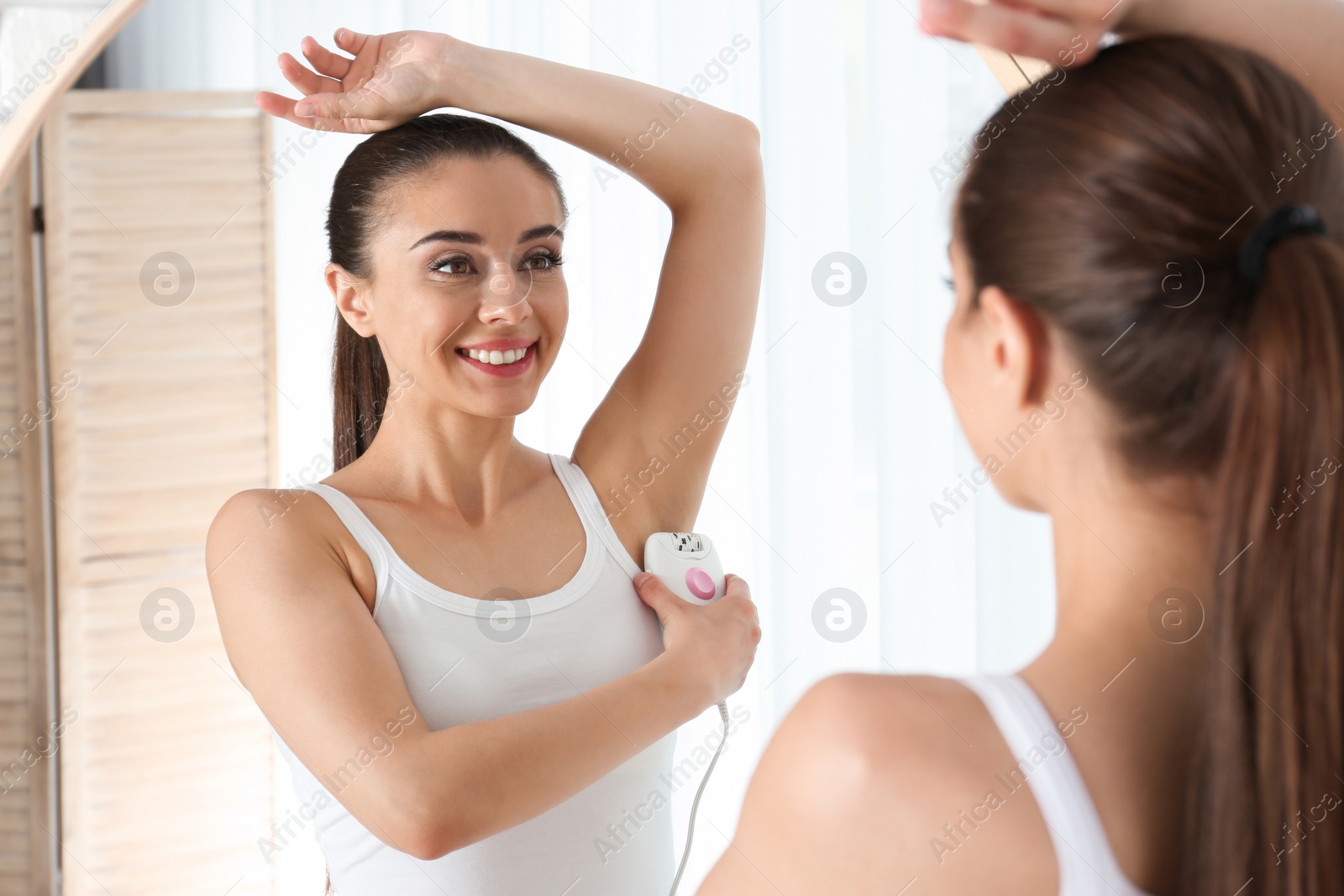 Photo of Young woman doing armpit epilation procedure near mirror at home