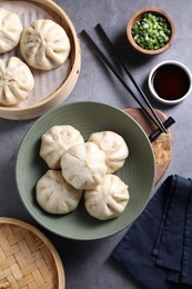 Photo of Delicious bao buns (baozi), chopsticks, soy sauce and green onion on grey table, flat lay