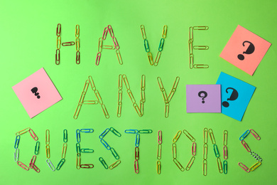 Photo of Phrase HAVE ANY QUESTIONS with paperclips and query marks on green background, flat lay