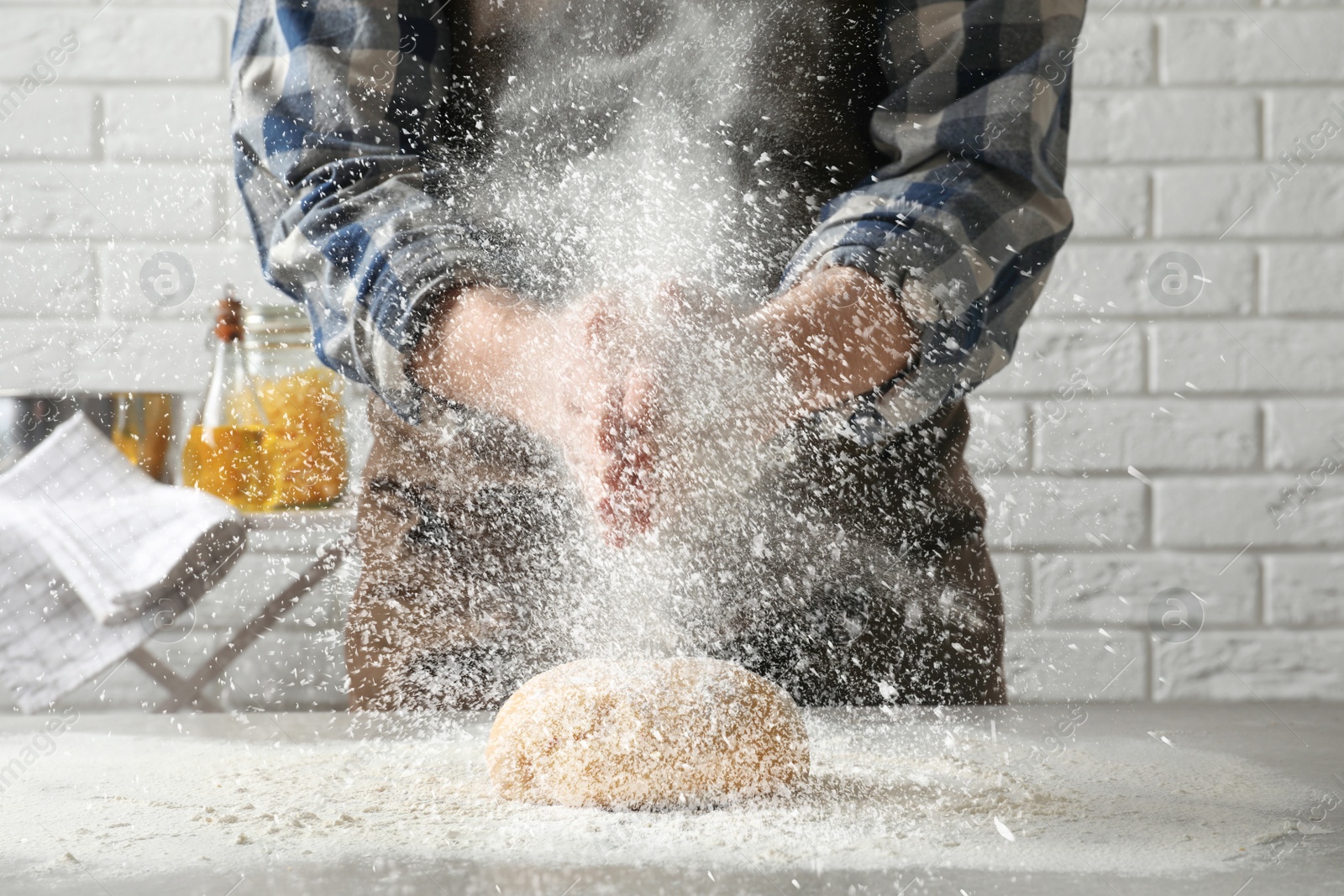 Image of Man sprinkling flour over dough on table in kitchen, closeup