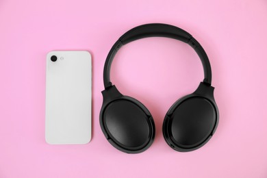 Modern wireless headphones and smartphone on pink background, flat lay