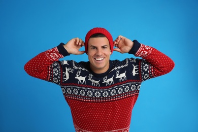 Handsome man in Christmas sweater and hat on blue background