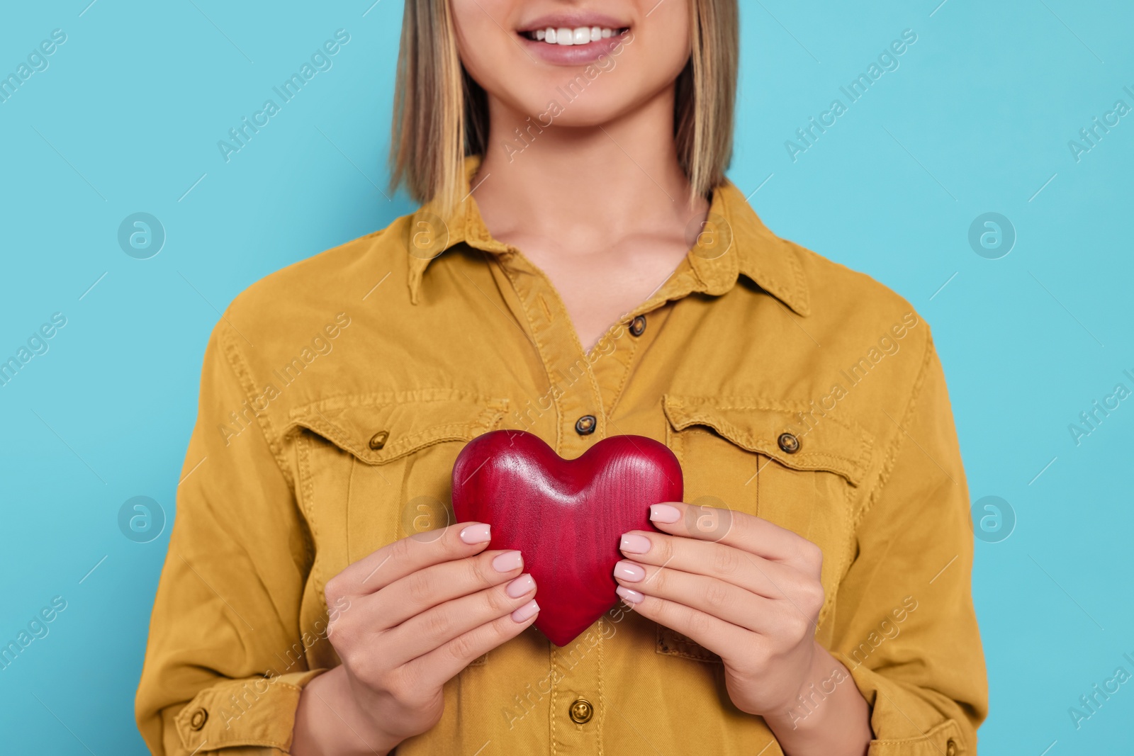 Photo of Young woman holding red heart on turquoise background, closeup. Volunteer concept