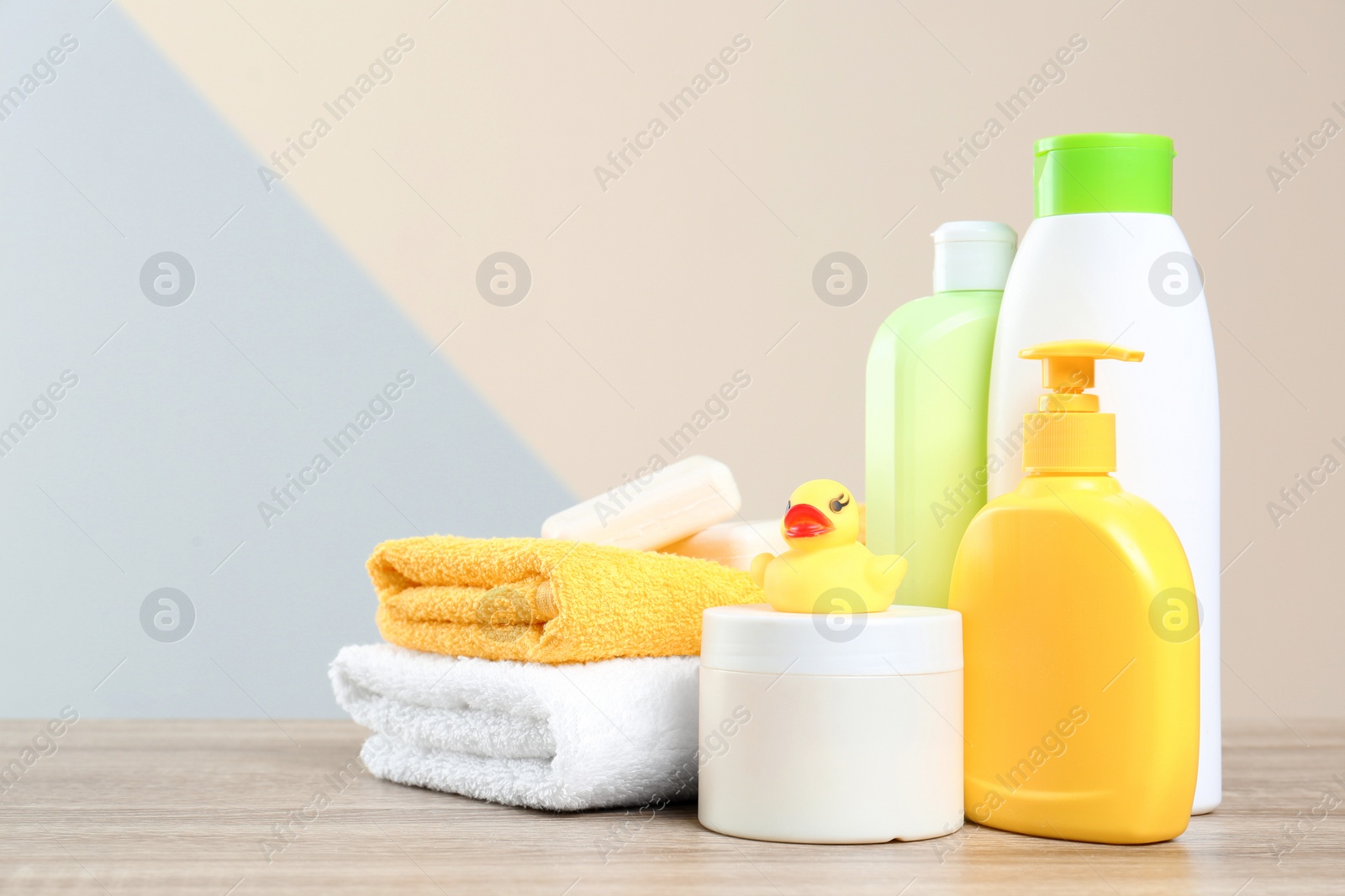 Photo of Baby cosmetic products, toy and towels on table against color background. Space for text