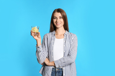 Young woman with glass of lemon water on light blue background