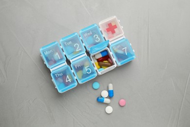 Photo of Plastic box with different pills on light grey stone table, flat lay