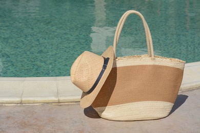 Stylish bag and hat near outdoor swimming pool on sunny day, space for text. Beach accessories