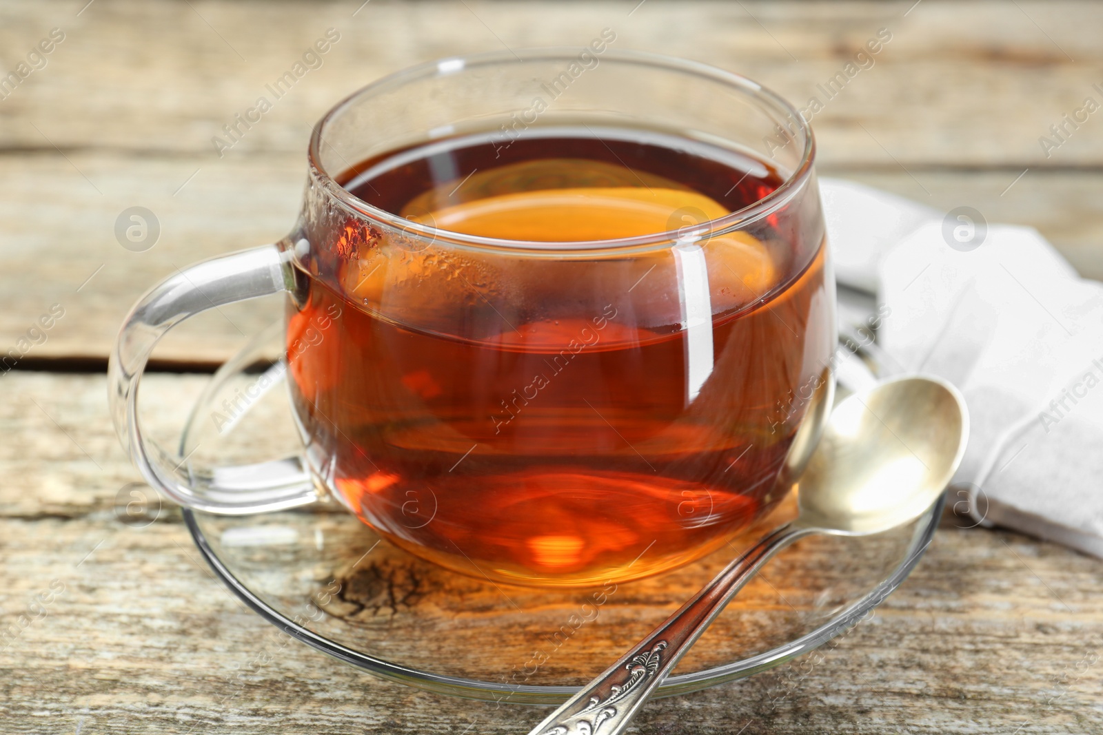 Photo of Aromatic tea in glass cup, spoon and teabags on wooden table