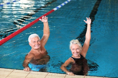 Photo of Sportive senior couple doing exercises in indoor swimming pool