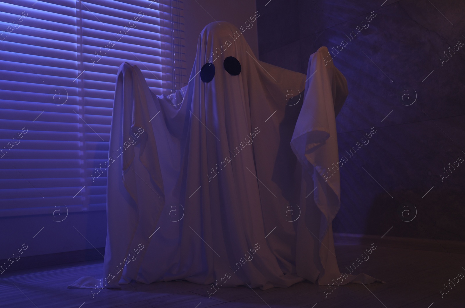 Photo of Creepy ghost. Woman covered with sheet near window in color lights