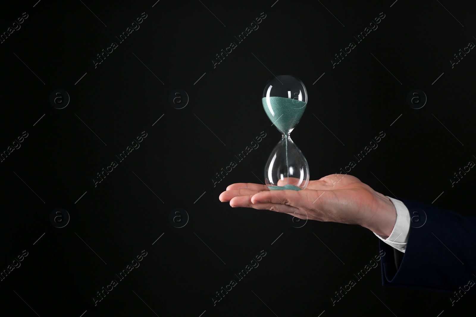 Photo of Closeup view of businessman holding hourglass on black background, space for text. Time management