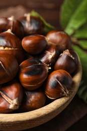 Photo of Delicious roasted edible chestnuts in wooden bowl on table, closeup