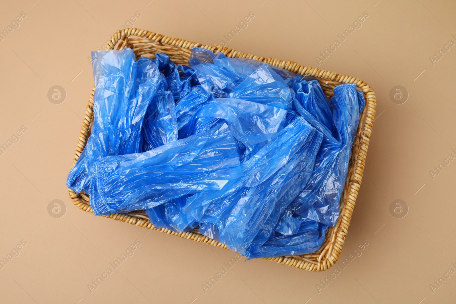 Photo of Blue medical shoe covers in wicker basket on beige background, top view