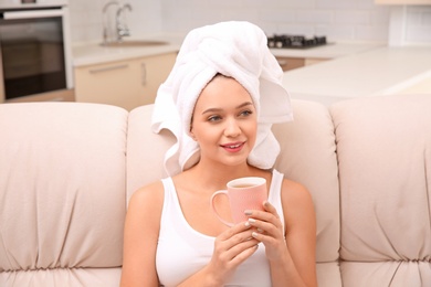 Photo of Beautiful woman with hair wrapped in towel sitting on sofa and drinking tea at home