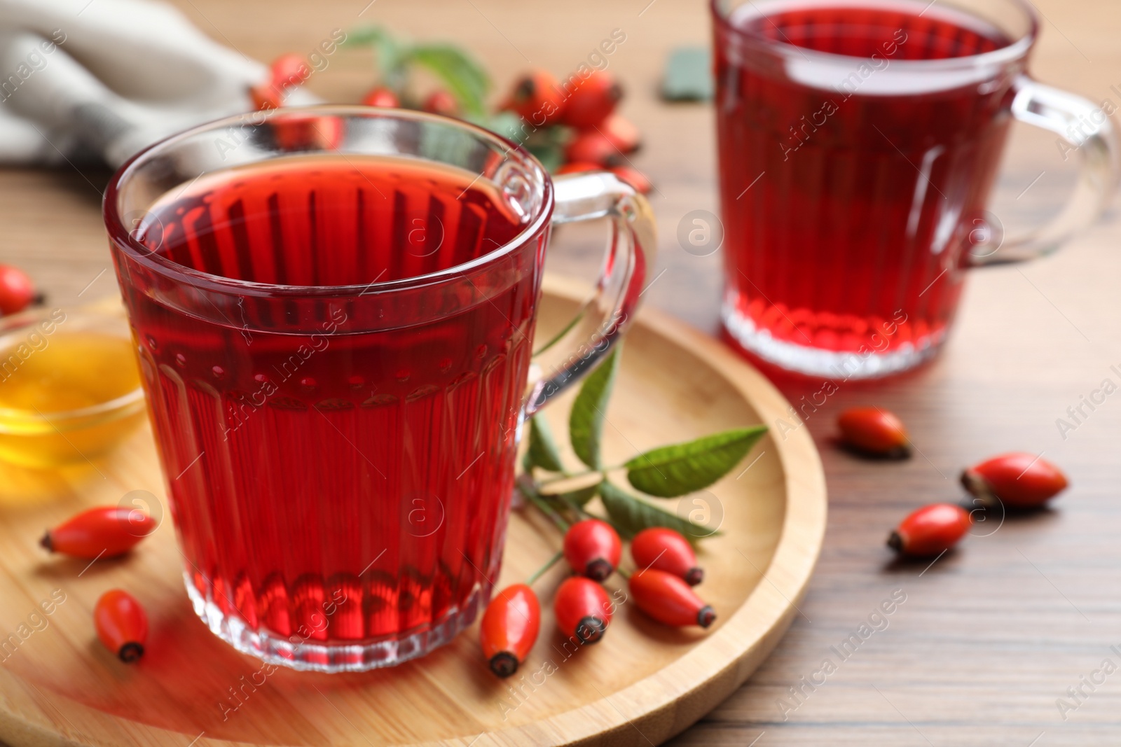 Photo of Fresh rose hip tea, honey and berries on wooden table, closeup