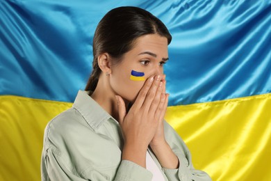 Photo of Sad young woman with clasped hands near Ukrainian flag