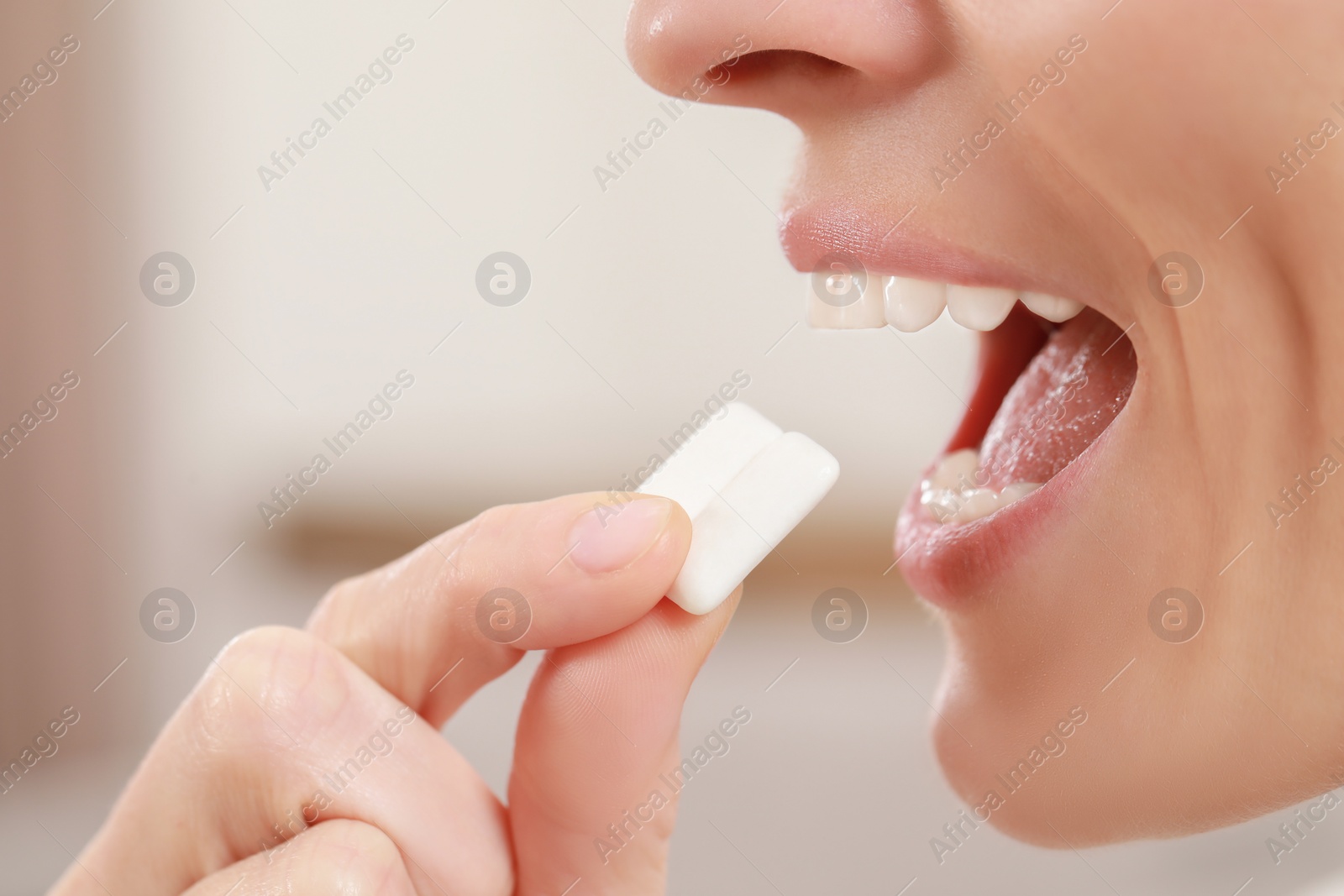 Photo of Woman putting chewing gum pieces into mouth on blurred background, closeup