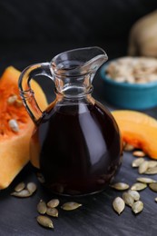 Photo of Fresh pumpkin seed oil in glass jug on dark grey table