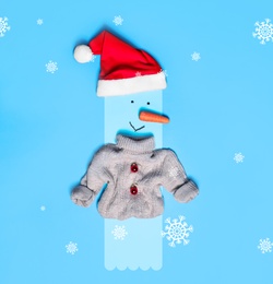 Image of Snowman with Santa hat and small sweater on light blue background, flat lay