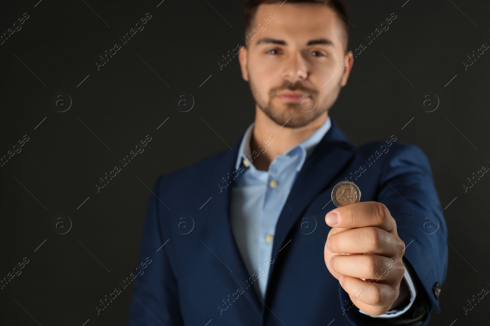 Photo of Young man holding coin against black background, focus on hand. Space for text