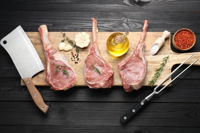 Photo of Fresh tomahawk beef cuts, spices and butcher tools on black wooden table, top view