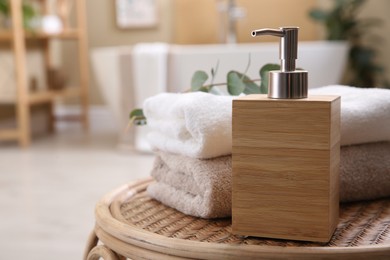 Photo of Wooden dispenser of liquid soap, clean towels and eucalyptus branch on wicker stool in bathroom. Space for text