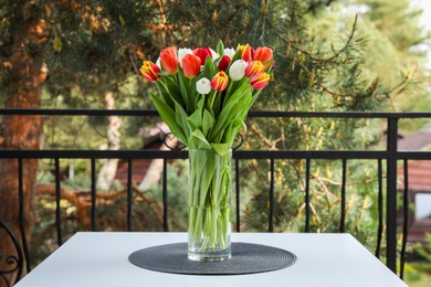 Photo of Beautiful colorful tulips in glass vase on white table at balcony