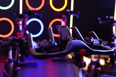 Photo of Modern exercise bikes in fitness club, closeup. Indoor cycling class