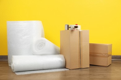 Photo of Bubble wrap rolls, tape dispenser and cardboard boxes on floor near yellow wall