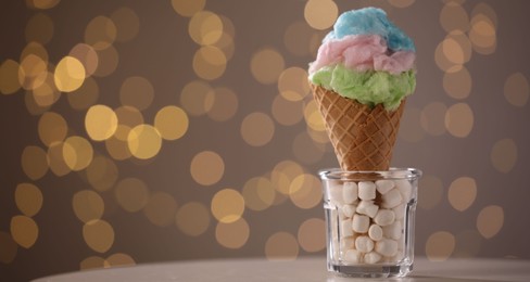 Sweet cotton candy in waffle cone on table against blurred lights, closeup. Space for text