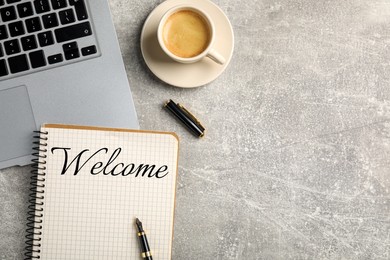 Image of Notebook with word Welcome, laptop and cup of coffee on grey table, flat lay. Space for text