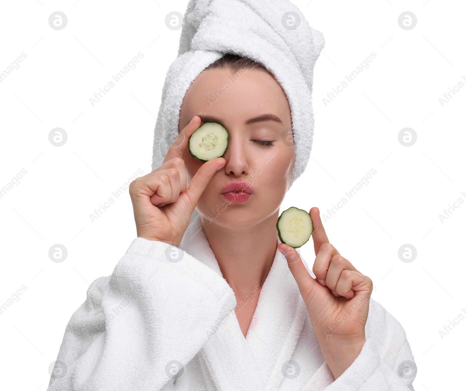 Photo of Beautiful woman in bathrobe covering eye with piece of cucumber and blowing kiss on white background