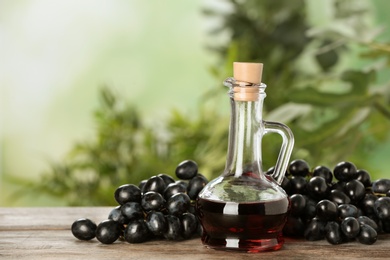 Photo of Glass jug with wine vinegar and fresh grapes on wooden table against blurred background