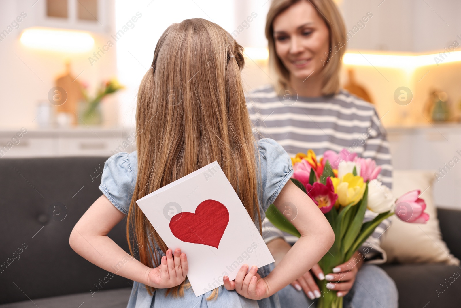 Photo of Little girl hiding greeting card for mom at home, selective focus. Happy Mother's Day