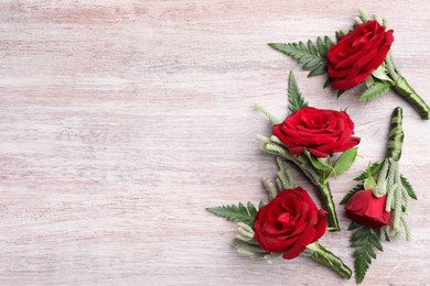 Many stylish red boutonnieres on light wooden table, flat lay. Space for text