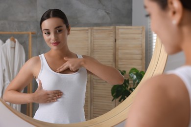 Photo of Beautiful young woman doing breast self-examination near mirror in bathroom