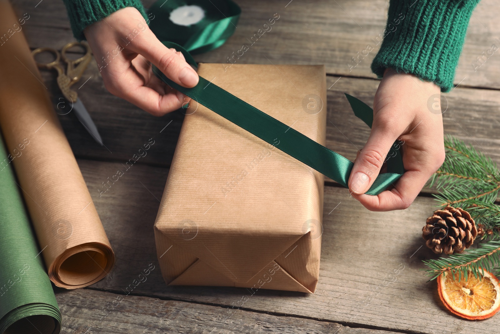 Photo of Christmas present. Woman tying ribbon around gift box at wooden table, closeup