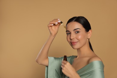 Photo of Young woman applying essential oil onto face against beige background. Space for text