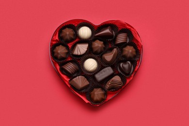 Heart shaped box with delicious chocolate candies on red background, top view