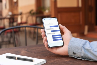 Image of Man texting via mobile phone at table outdoors, closeup. Device screen with messages