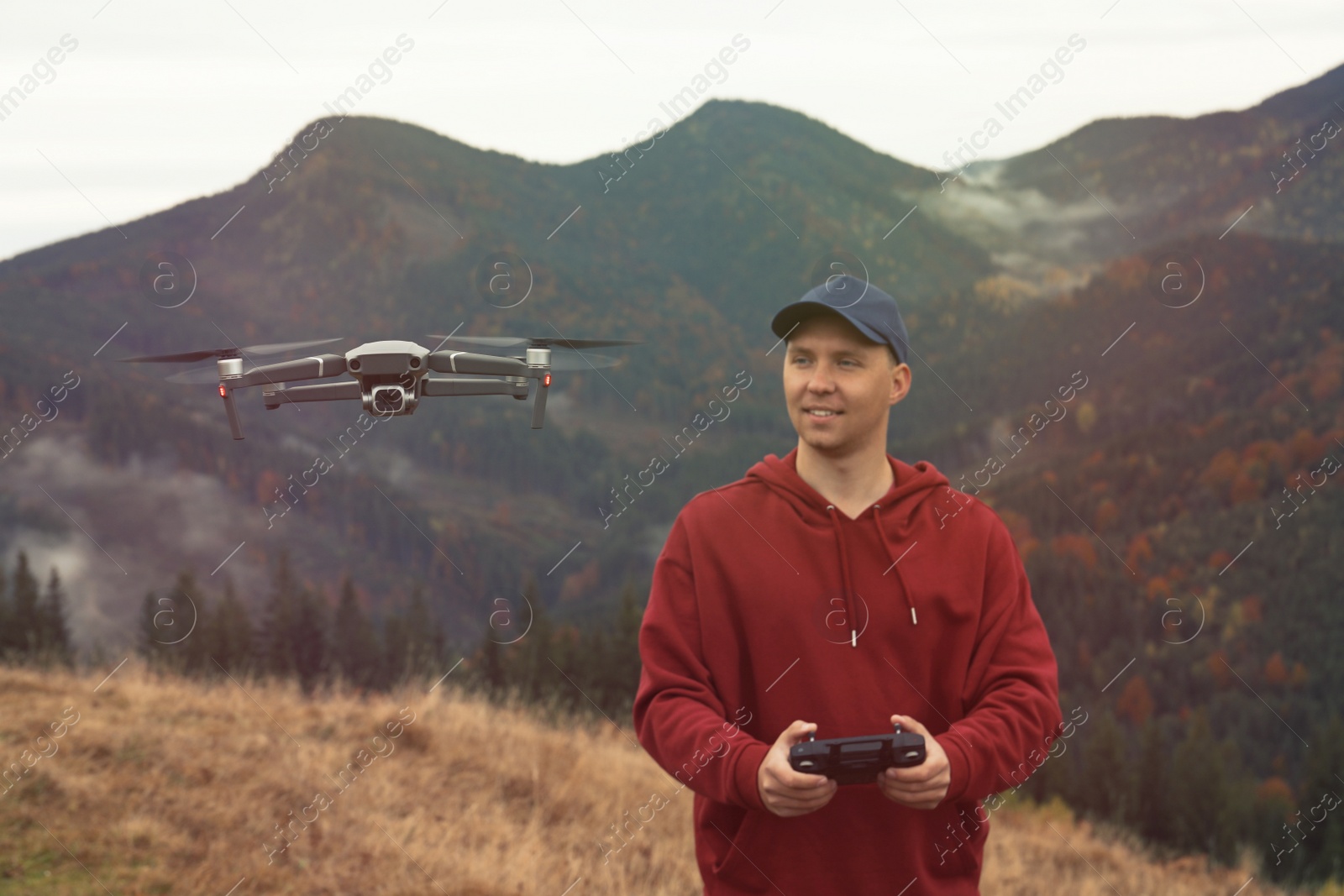 Photo of Young man operating modern drone with remote control in mountains