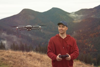 Photo of Young man operating modern drone with remote control in mountains