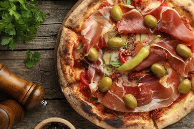 Tasty pizza with cured ham, olives, sun-dried tomato and pepper on wooden table, top view